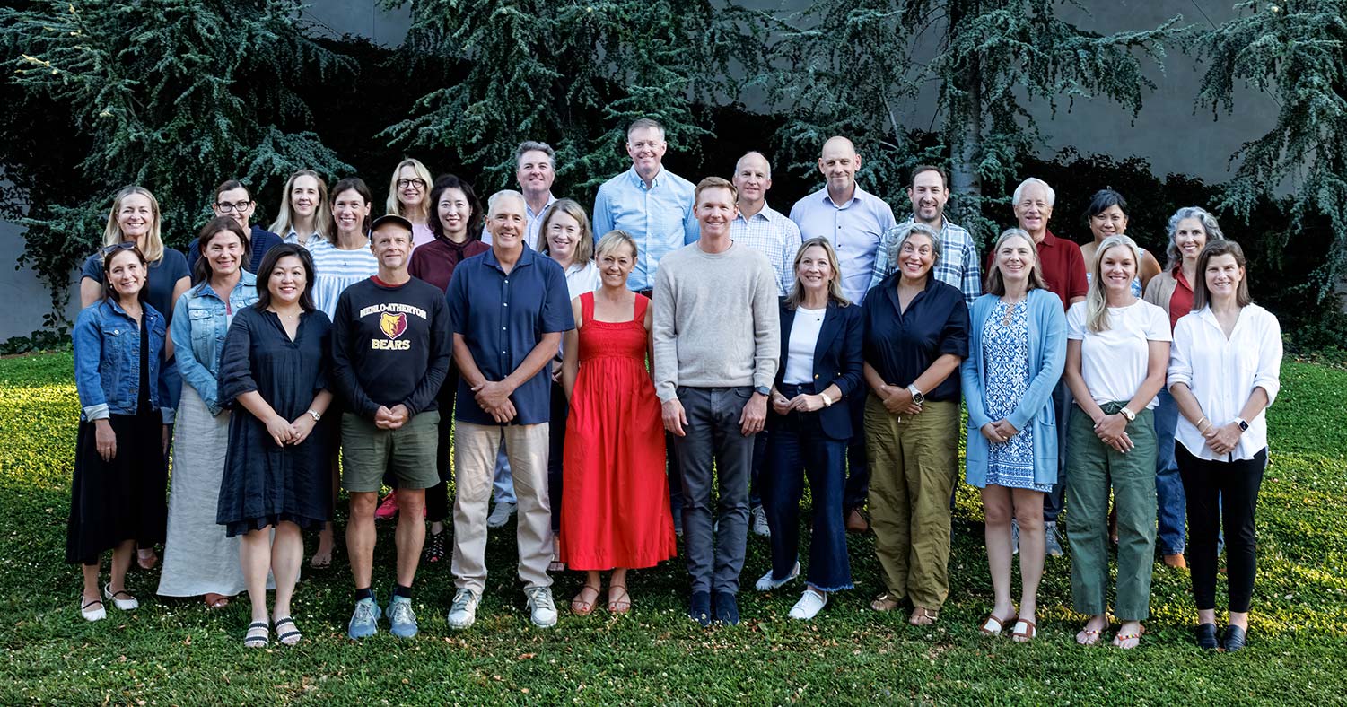 A large group of about 30 board members smiles, standing in the grass